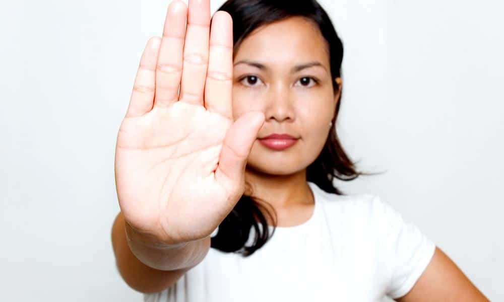 young woman in white shirt holding up hand defensively to back off