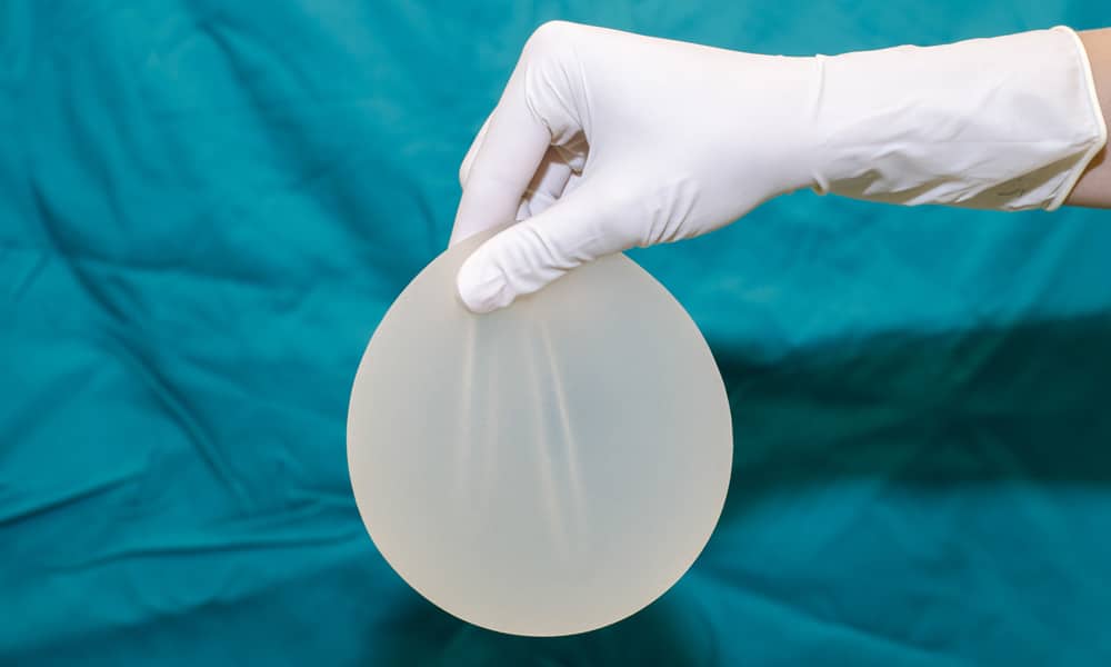 silicone breast implant held by white gloves